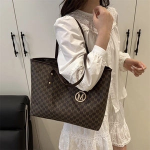 Brown leather tote bag with M-letter pattern and metal charm on a white lace dress