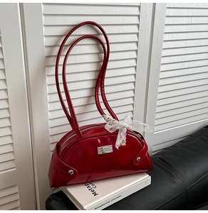 Detail showing red patent leather handbag with lace bow and sleek metallic plaque