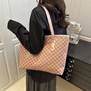 Pink minimalist tote bag with monogram print and gold M-logo charm in a cozy indoor scene