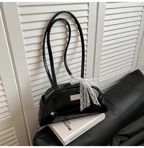 Detail of minimalist black patent leather shell bag with lace bow and metal plaque