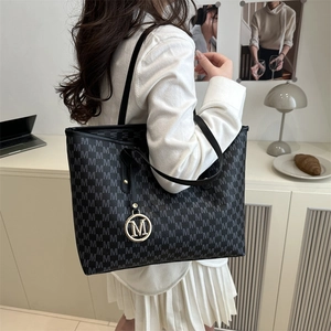Chic black tote bag with M-letter monogram print and gold pendant on a desk