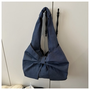 Détail d'un sac à épaule en jean avec un grand nœud décoratif et des surpiqûres orange
