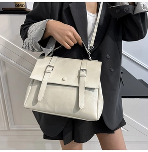 Detail view of a cream vintage messenger bag with silver buckles worn with a black blazer