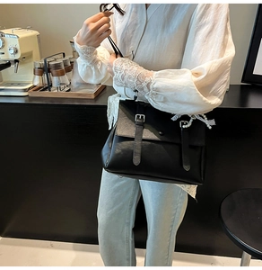 Detail of vintage black matte leather satchel with elegant pearl and lace charm accessories