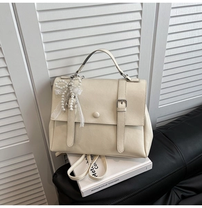 Detail of off-white retro satchel featuring premium leather texture and pearl lace bow charm
