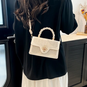 Beige woven crossbody bag with floral gold lock and braided handle shown on a model