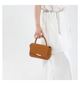 Detail of caramel leather handbag with gold bar buckle and top handle held by a model