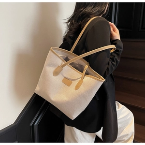 Detailed view of canvas tote bag with brown leather handles worn over shoulder by model