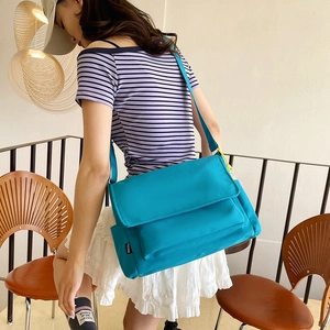 Large turquoise nylon messenger bag for casual outdoor use shown on model in a cafe