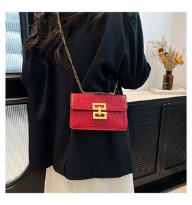 Detalle de bolso bandolera rojo con grabado de cocodrilo, cierre dorado y cadena metálica