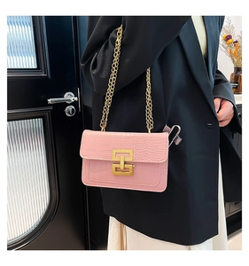 Detalle de bolso bandolera rosa con grabado de cocodrilo y cierre de doble anilla dorada