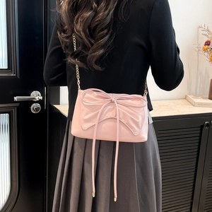 Sac bandoulière rose avec nœud et chaîne dorée, porté par un mannequin en intérieur