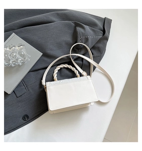 Detail of white leather handbag featuring a unique white and gold twisted top handle design