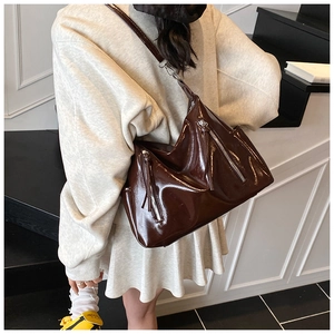 Detail view of large dark brown patent leather tote bag with stylish metal zippers and strap
