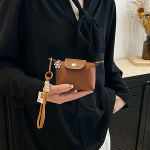 Mini nylon tas in bruin met leren flap en wit bloemvormig bedeltje aan koord