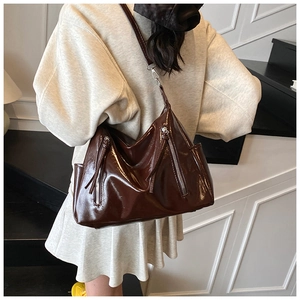 Detail of dark brown glossy underarm bag featuring decorative dual zippers and shoulder strap