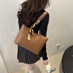 Brown faux leather tote bag with decorative scarf on handle worn by a model