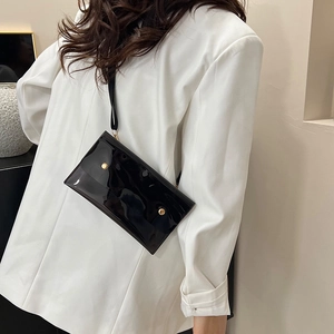 Minimalistische schwarze Lackleder-Umschlagtasche mit Goldnieten auf weißem Blazer getragen