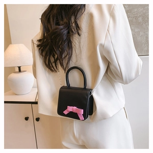 Vue arrière d'un mini sac carré noir avec un nœud rose et une bandoulière en chaîne argentée