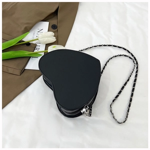 Macro shot of black heart-shaped crossbody bag with silver chain strap on white fabric