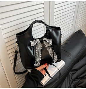 Close-up of black PU leather handbag featuring elegant white lace bow decoration