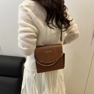 Brown leather crossbody square bag with metal chain detail shown on a female model