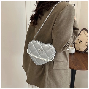 Silver heart-shaped quilted handbag with pearl trim worn by a model in a brown blazer