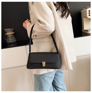 Close-up of black woven underarm bag with elegant gold rectangular metal clasp lock