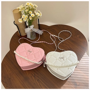 Close-up of heart-shaped quilted handbags with pearls and bow accent on a wooden table