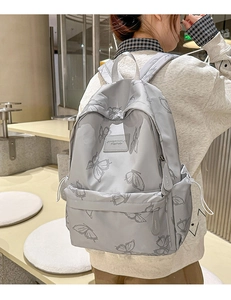 Detail of light grey butterfly print backpack on model in casual indoor setting