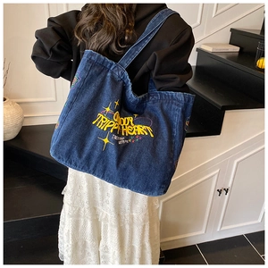 Detail van blauwe denim draagtas met geel borduursel en ruim ontwerp met schouderbanden