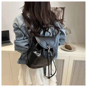 Detail of a minimalist black faux leather backpack with metallic hook and drawstring closure