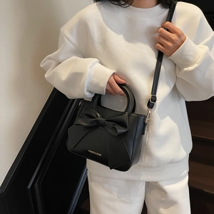 Minimalist black leather handbag with large bow decoration and round handle on model