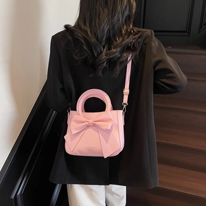 Pink PU leather handbag with a large bow and adjustable strap carried by a model