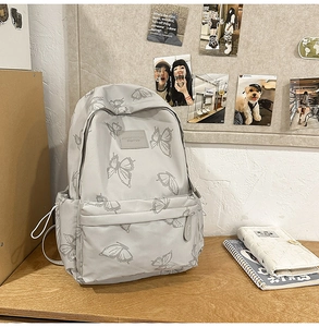 Close-up of butterfly print detail and front zipper pocket on the grey nylon backpack