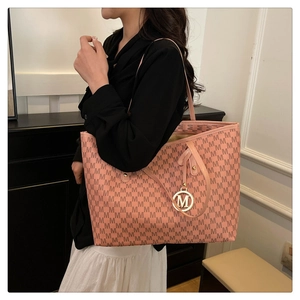 Detail of pink tote bag with M-pattern and gold charm worn by a model in a minimal setting