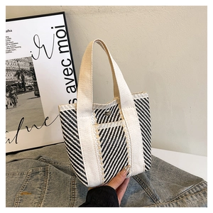 Detail of woven tote bag featuring black and white stripes with canvas handles and snap button