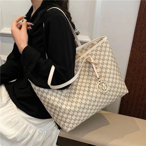Large beige tote bag with M-letter pattern and metal charm shown on model