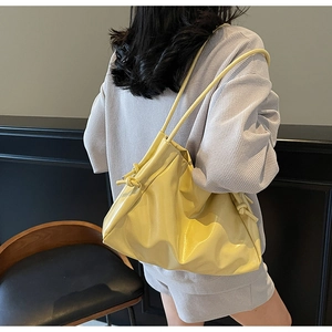 Detail view of a glossy yellow tote bag with knotted drawstring handle on model shoulder