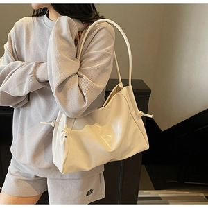 Detail showing the cream glossy shoulder bag with knot decoration and shiny finish