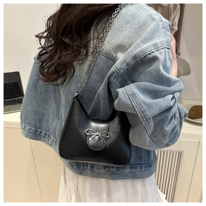 Détail du sac sous le bras en forme de croissant noir avec nœud argenté et chaîne fine