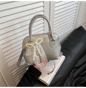 Close-up of silver shell bag with pearly bow, heart pendant and lace trim detail