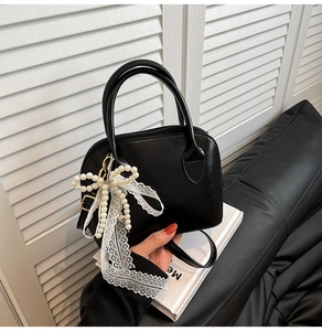 Macro shot of black shell bag with pearl bow pendant and white lace ribbon detail