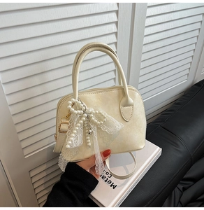Close-up of beige shell handbag featuring decorative lace bow and pearl charm details
