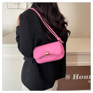Detail view of the bright pink shoulder bag with a gold buckle worn by a model in a black suit
