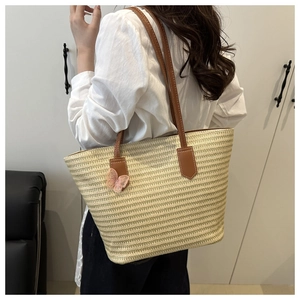 Close-up of woven straw tote bag with brown leather straps and pink butterfly charm