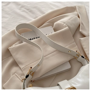 Detail of white faux leather hobo bag with adjustable gold hardware on a beige blazer
