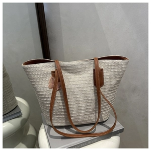 Detail of woven straw tote bag featuring pink butterfly embroidery and brown shoulder strap