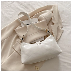 Close-up of white glossy leather tote bag with gold metal hardware on beige suit