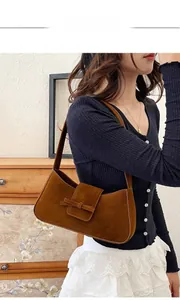 Detail showing brown suede underarm baguette bag with a stylish 3D bow and flap closure